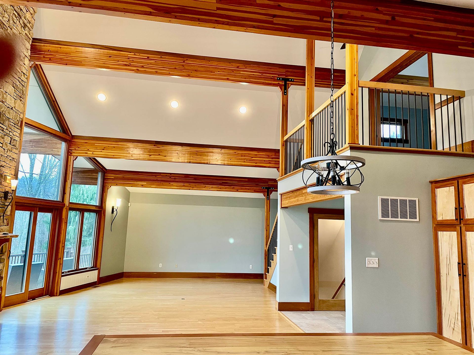Spacious room with wooden beams, hardwood floor, large windows, and a loft area.