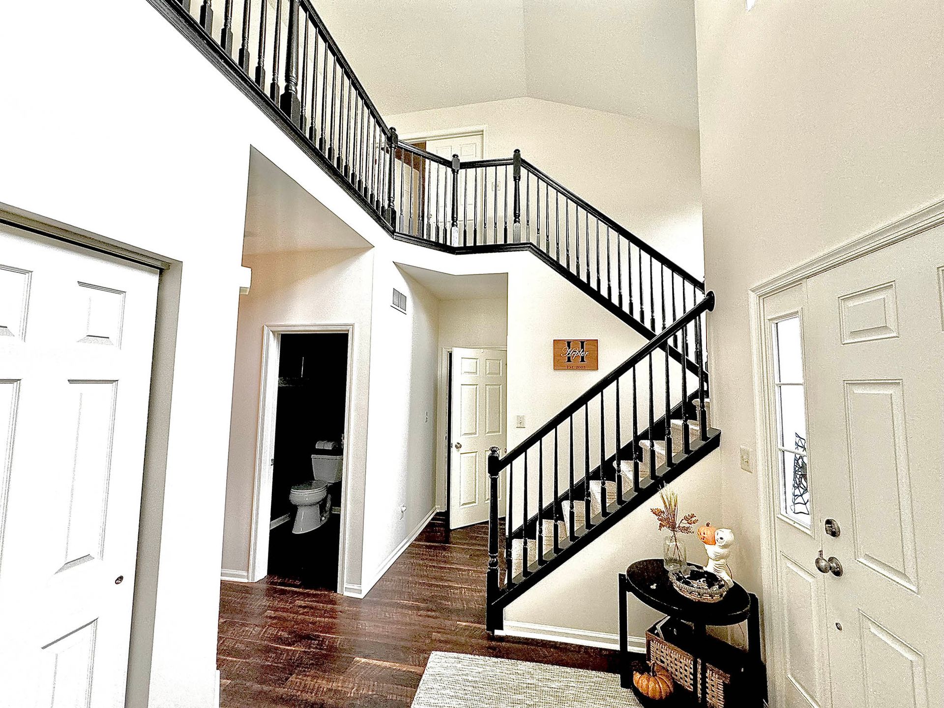Interior of a home with a staircase, white walls, and a dark wooden banister.
