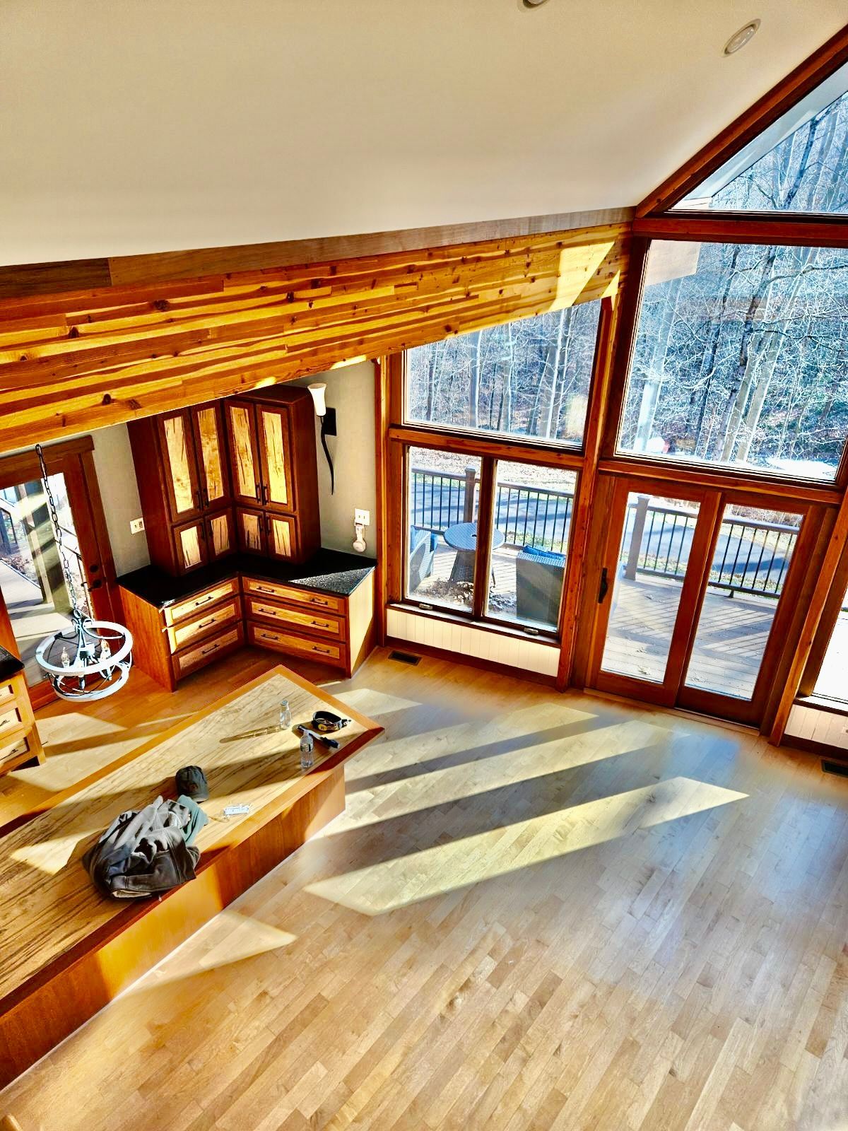 Spacious wood-paneled room with large windows overlooking a deck and forest. Natural light floods the room.