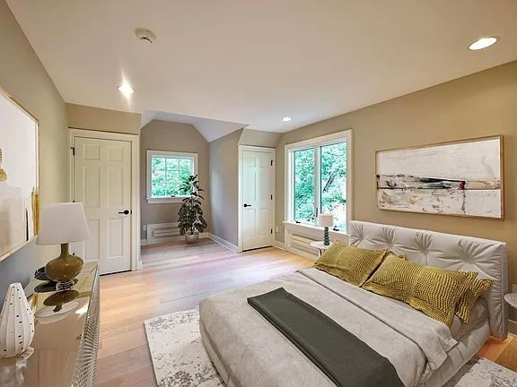 Bedroom with light-colored walls, bed, windows, artwork, and dresser. Neutral tones with a bright, airy feel.