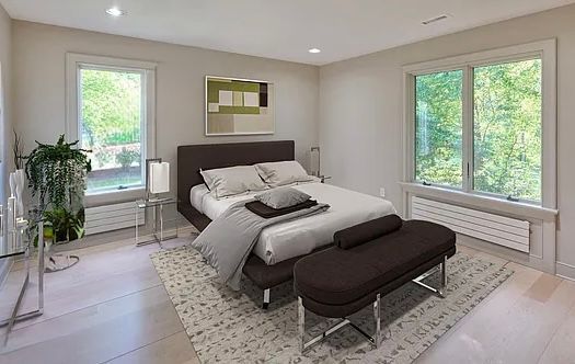 Bedroom with bed, bench, rug, two windows, and neutral walls.