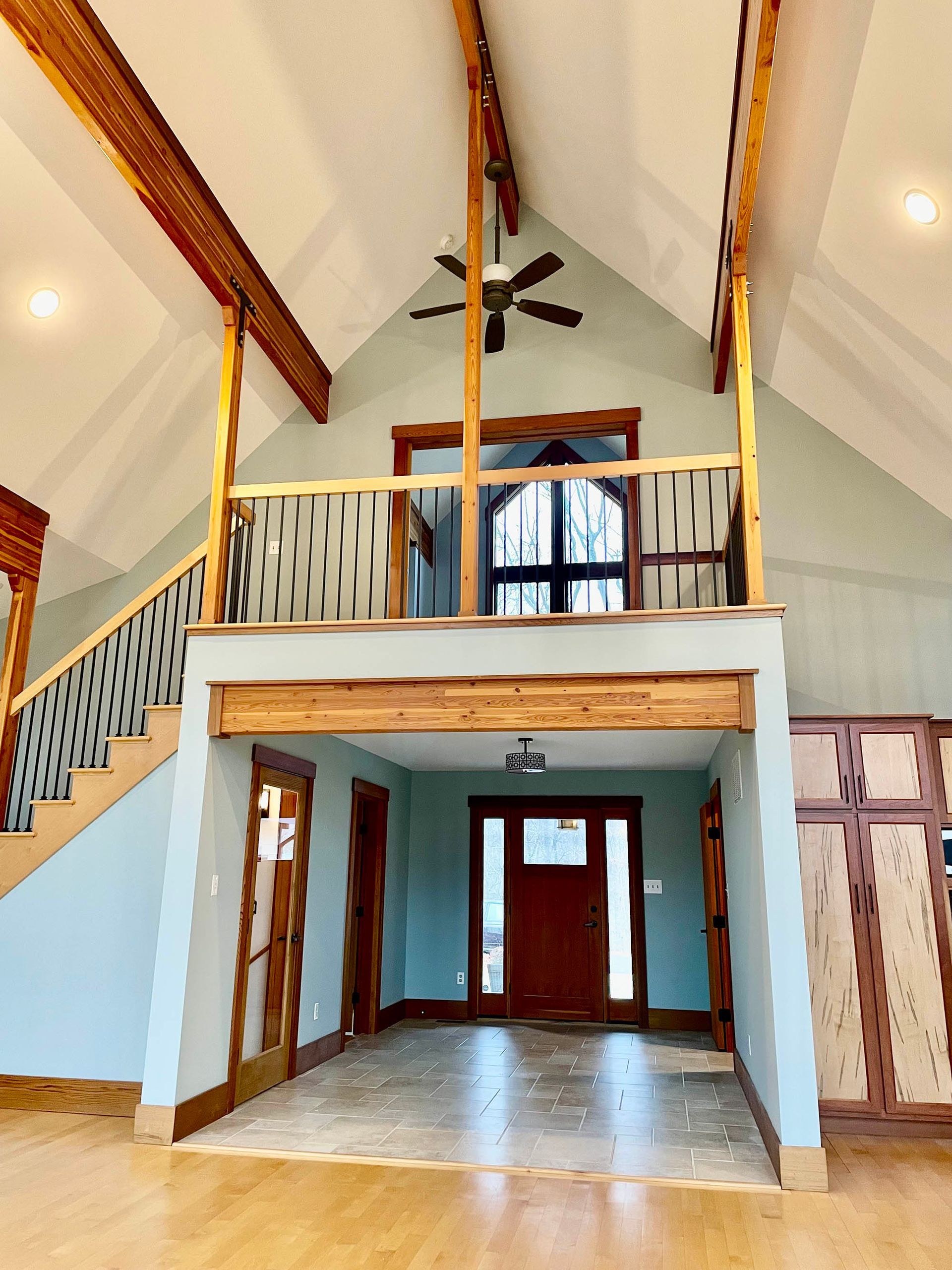 Interior view of a house with a loft, wood accents, high ceilings, and light blue walls.