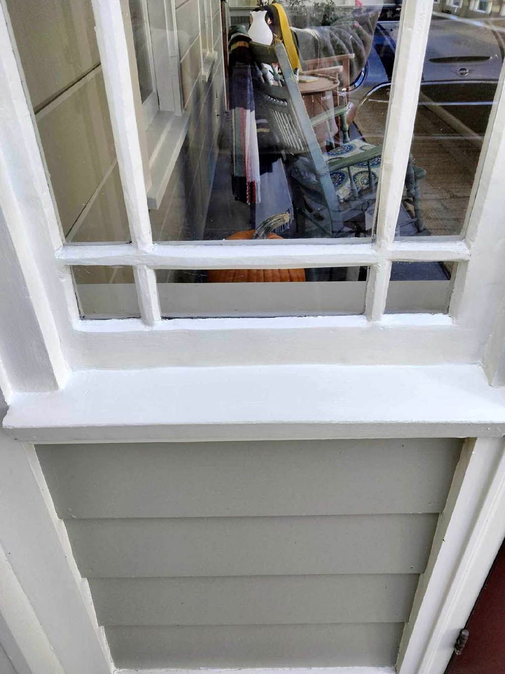 Window with white frame and light gray siding below. A person is visible through the glass.