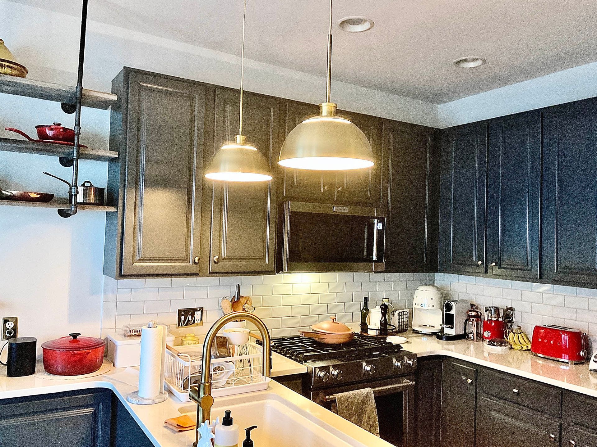 Kitchen with dark gray cabinets, white backsplash, brass light fixtures, and stainless steel appliances.
