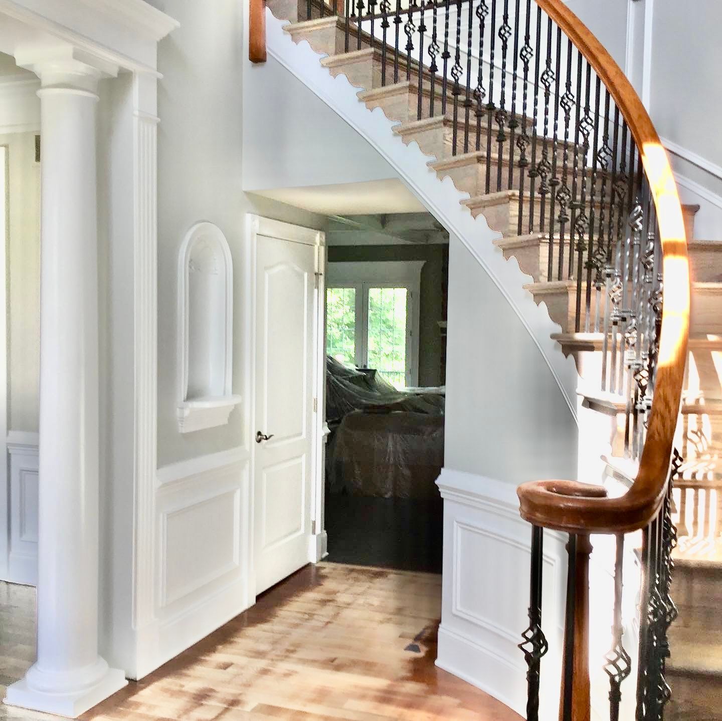 Interior with staircase, wooden floors, white trim, and a door opening to another room.