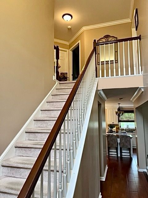 Staircase with light carpet and wooden railing. View of a second-floor hallway, and the kitchen below.