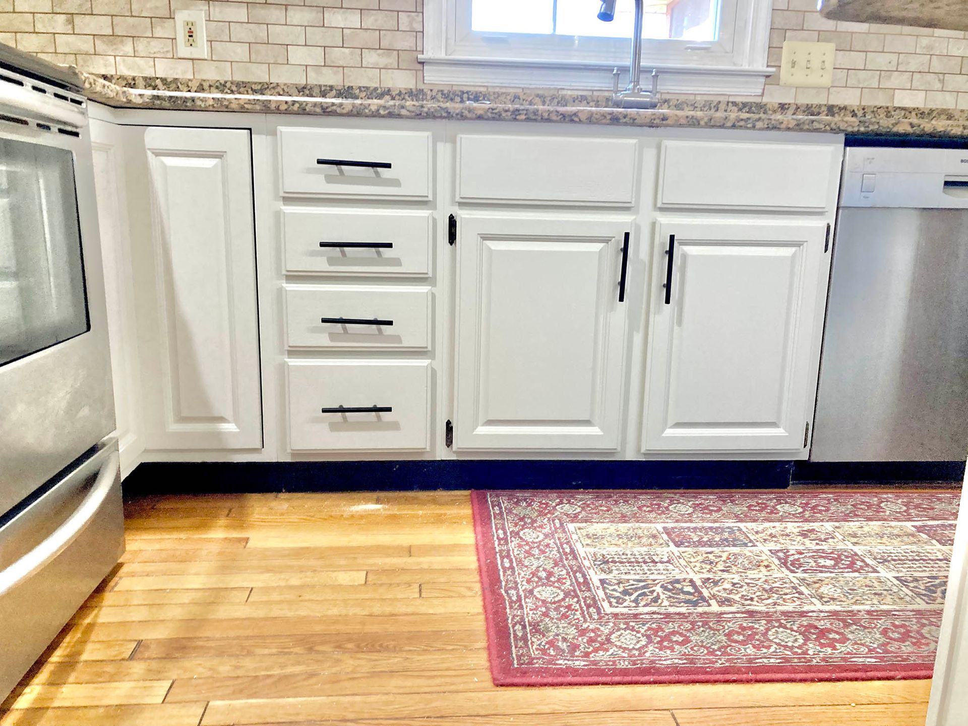 White kitchen cabinets with black handles, a stainless steel dishwasher, and a rug.