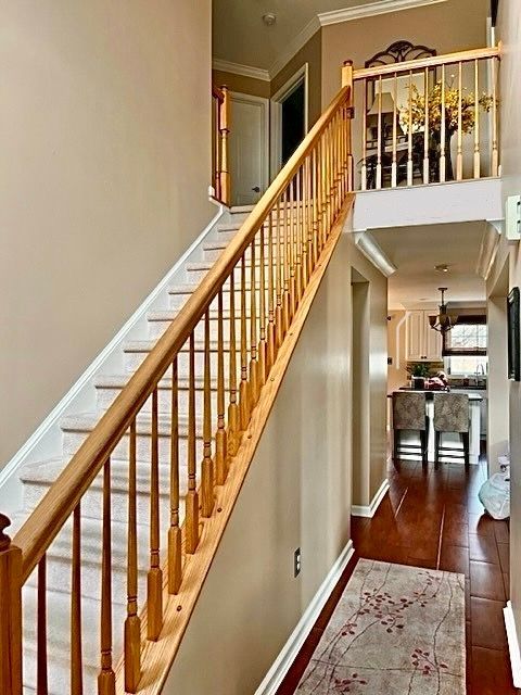 Wooden staircase with beige walls, leading to a second floor. A hallway with dining area is visible.