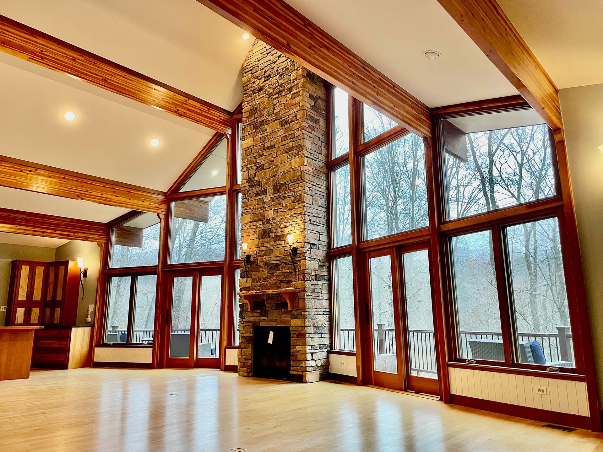 Spacious room with large windows, wooden beams, a stone fireplace, and light wood flooring.