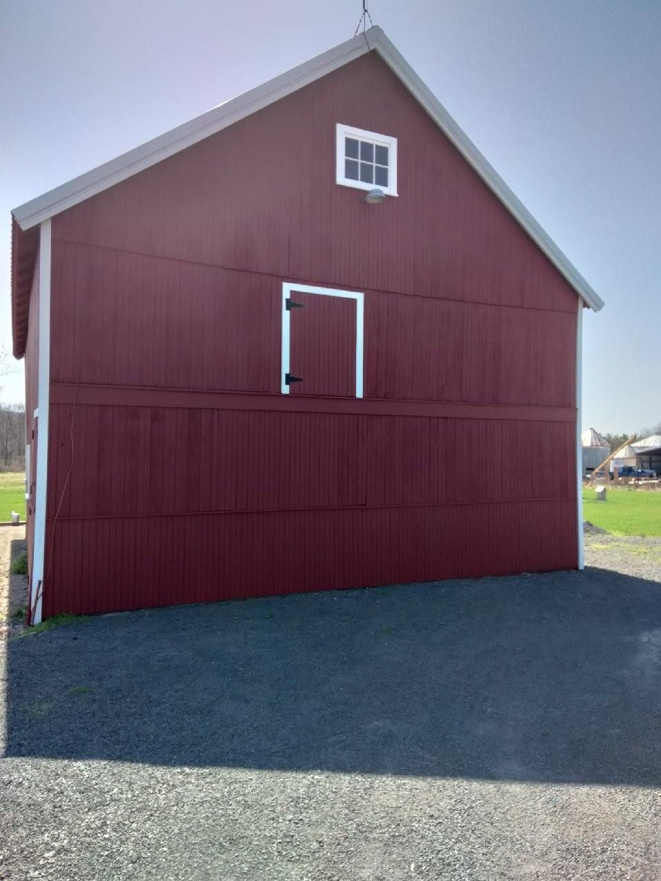 Red barn with white trim, door, and small window. Gravel in front, blue sky.