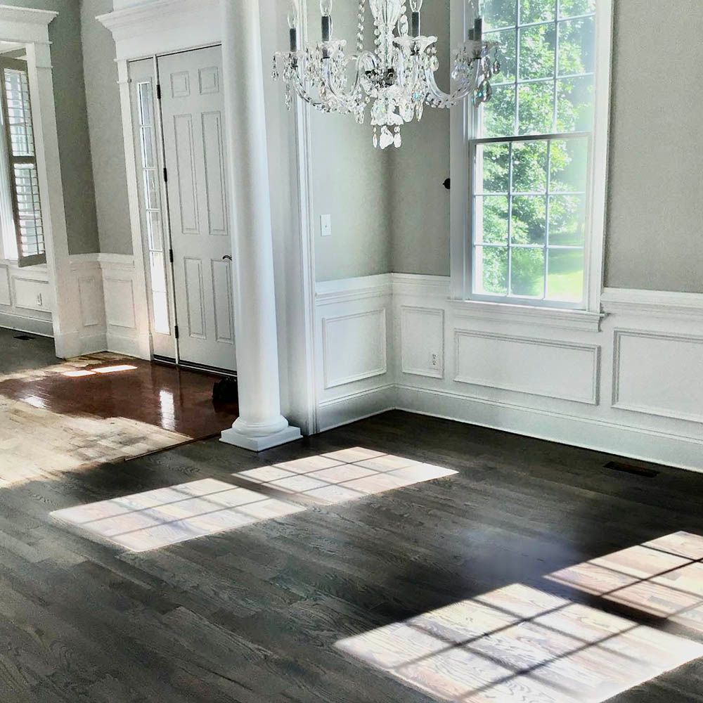 Sunlight through windows casts rectangular patterns on dark wood floors of a bright room with white trim and a chandelier.