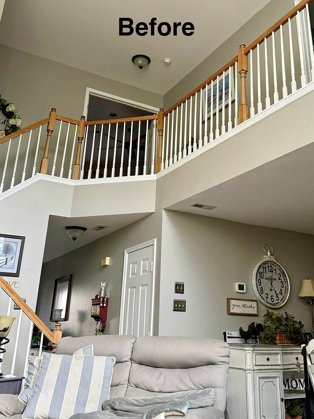 Before image of a two-story foyer with staircase, beige walls, white spindles, and light wood railings.