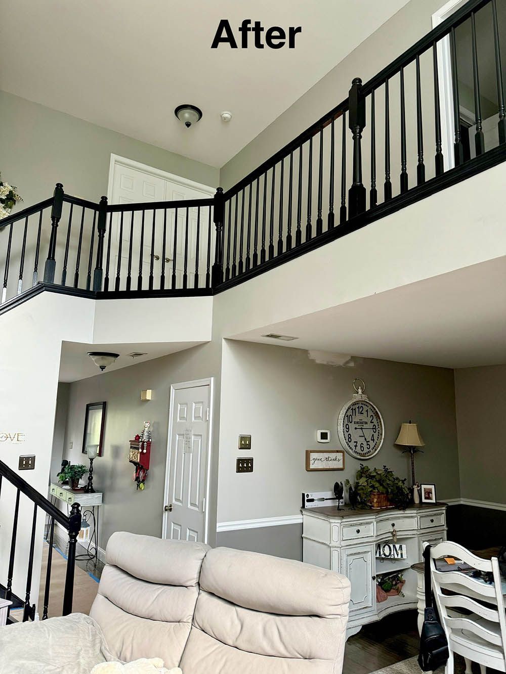 Interior view of a two-story foyer with black railing. Gray walls and white trim. Living room with a white cabinet.