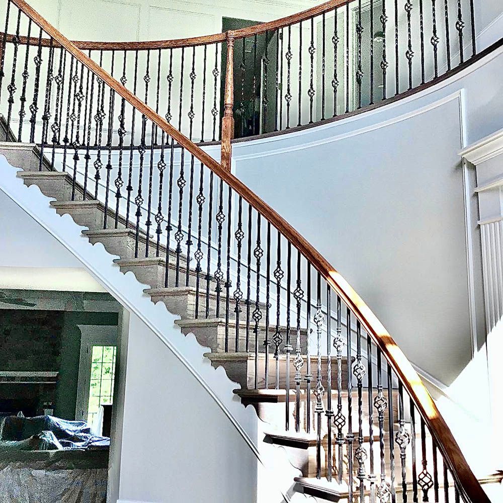 Grand staircase with wooden handrails and black iron balusters, in a light-colored interior.