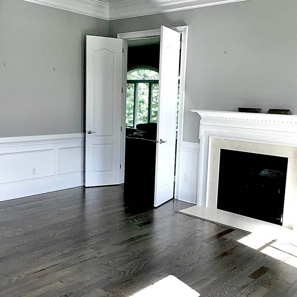 Empty room with fireplace, white molding, gray walls, and hardwood floor.