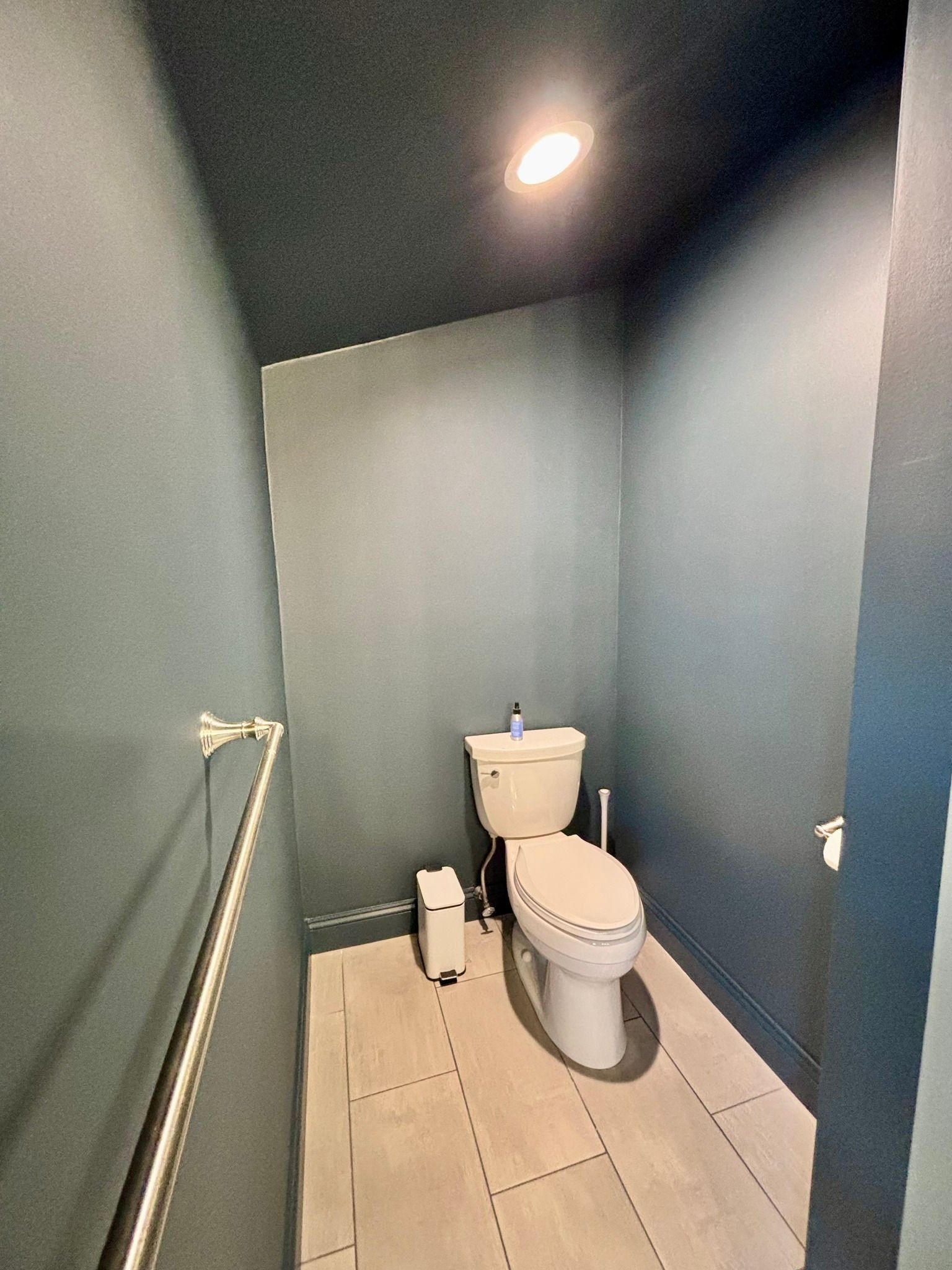 Small blue powder room with a toilet, paper dispenser, and towel rack.