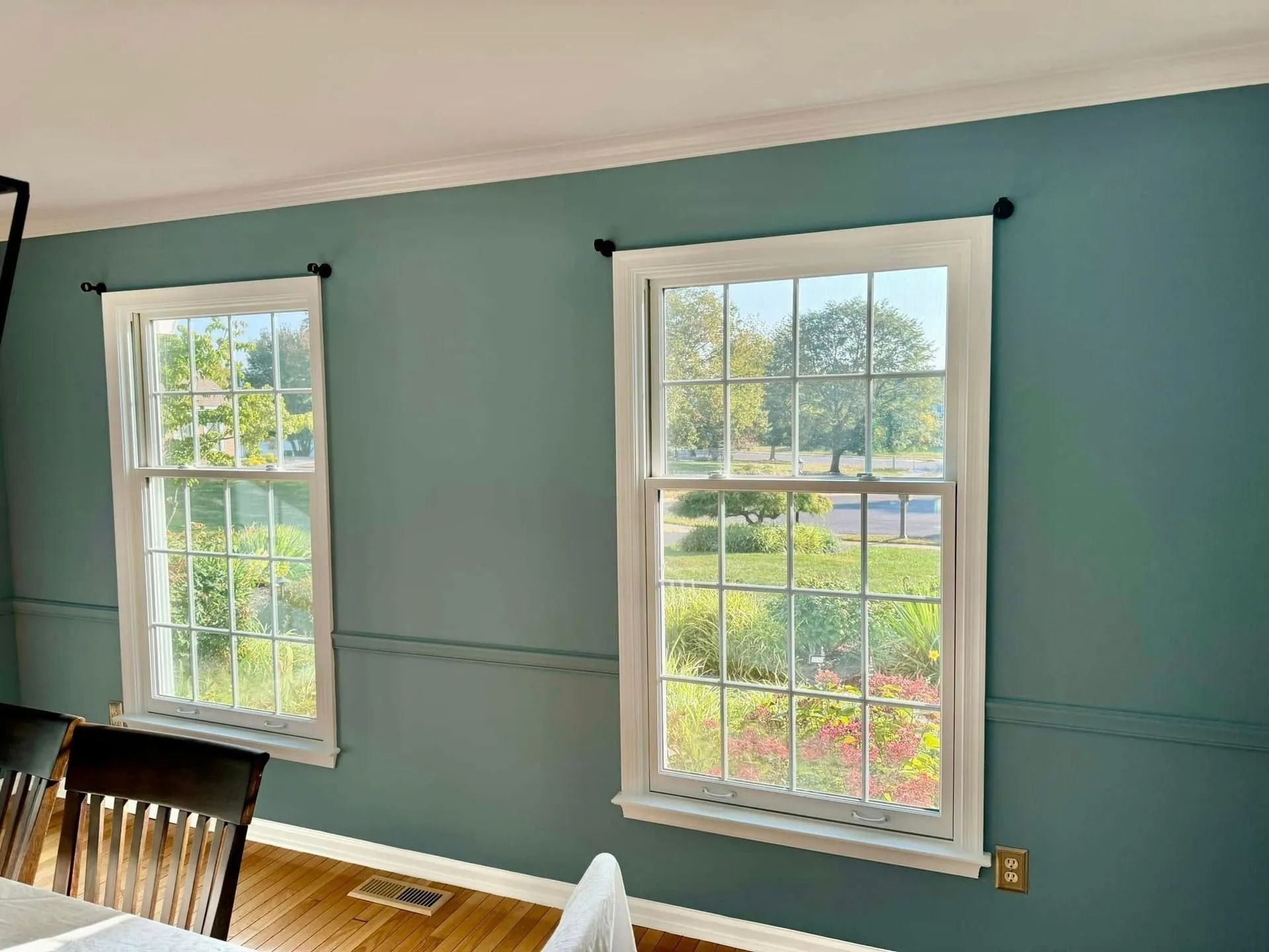 Two white-framed windows on a teal wall, casting light on a wood floor and furniture.