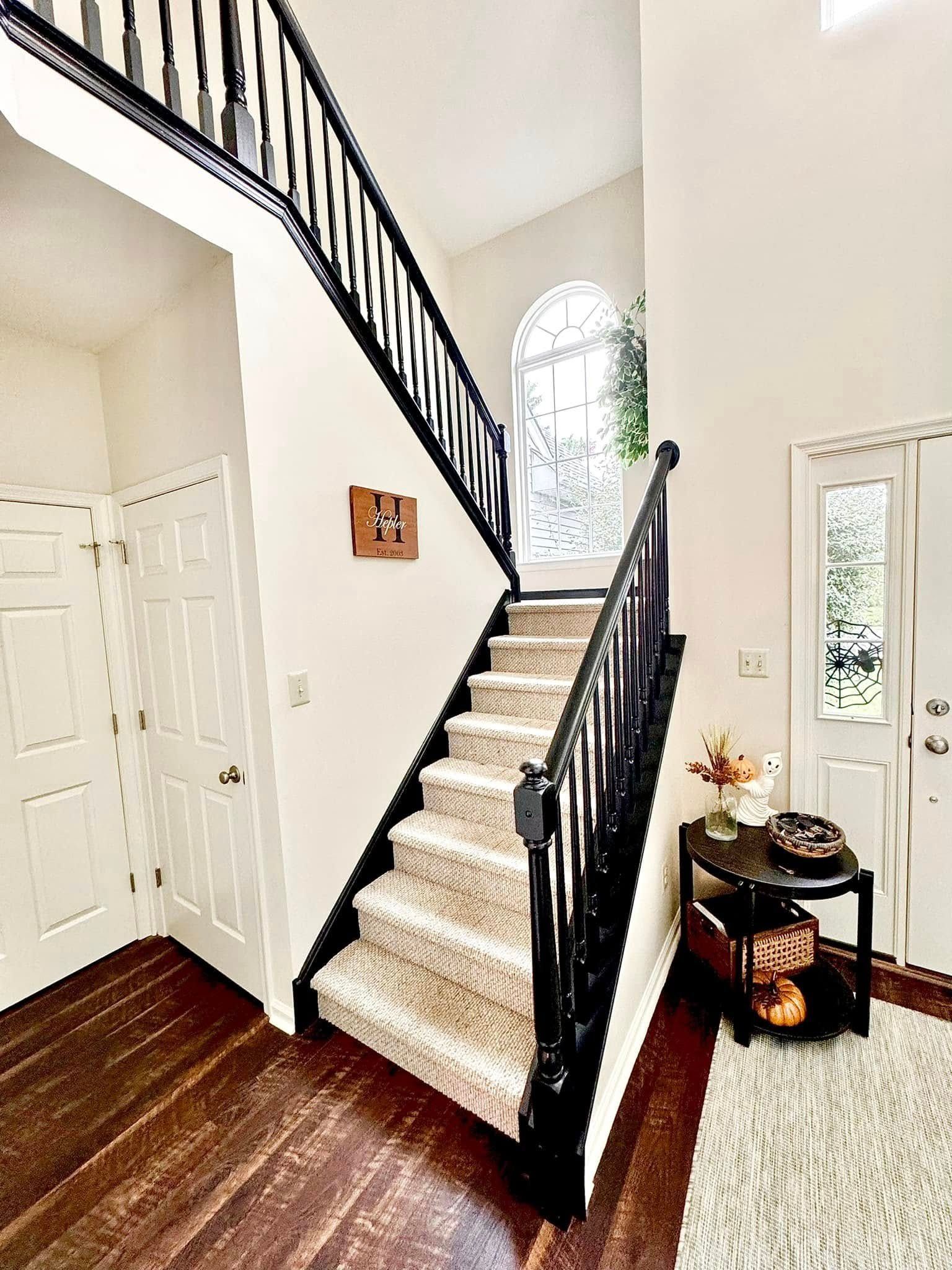 Staircase with black railing, carpeted steps, and wood floor. A table with decor sits at the bottom.