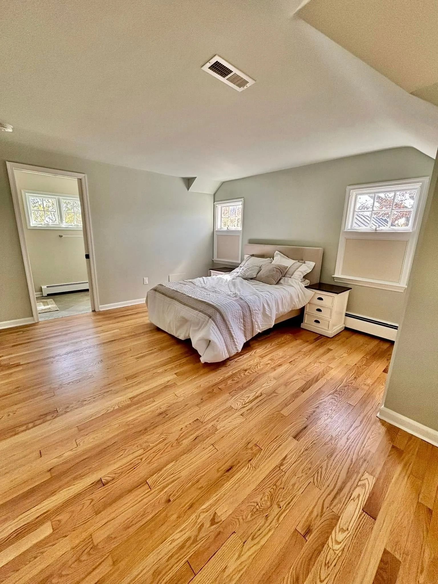 Bedroom with hardwood floors, bed, nightstand, and window. Door to bathroom visible.