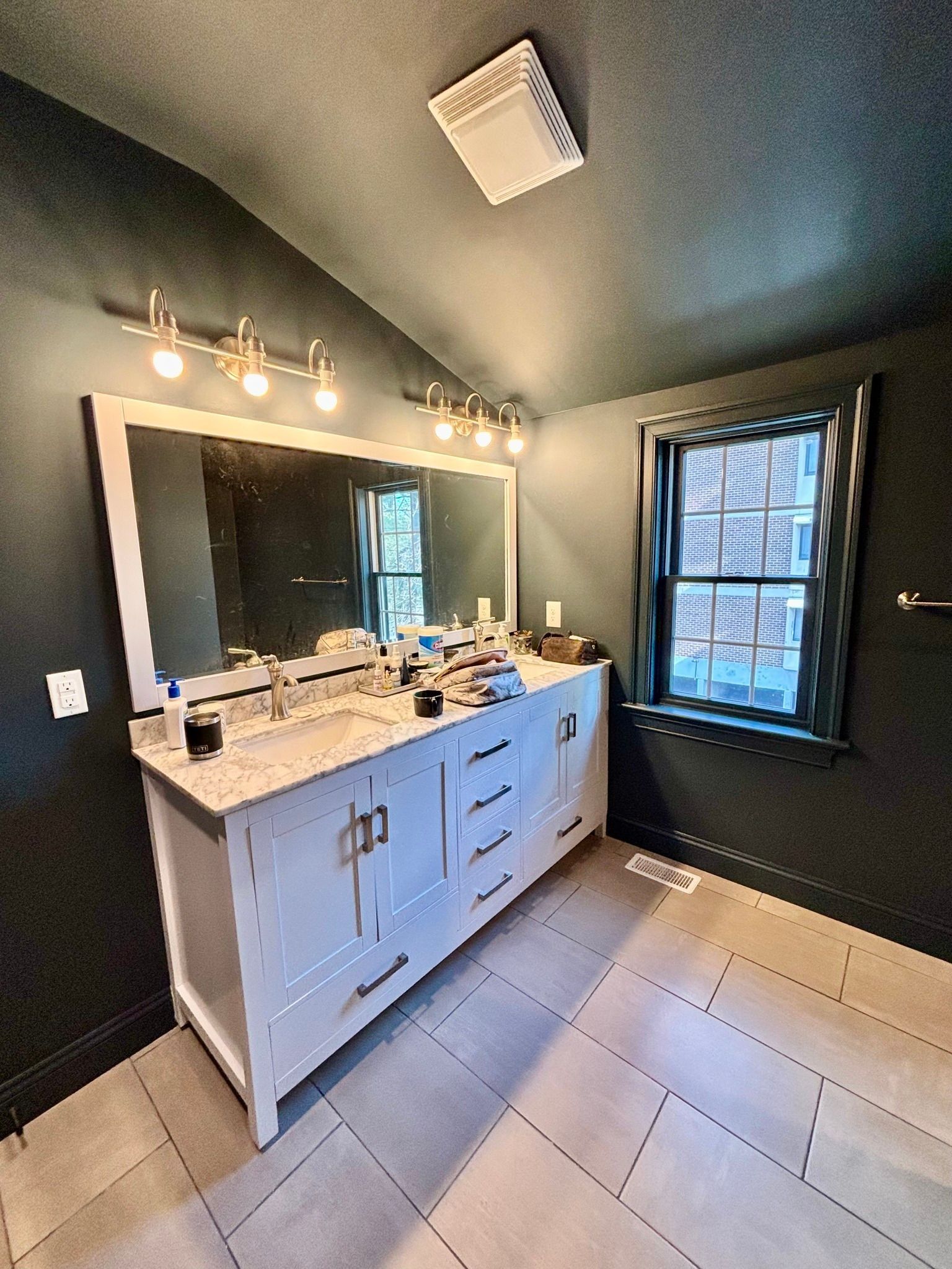 Bathroom with white vanity, large mirror, and dark walls; window on the right.