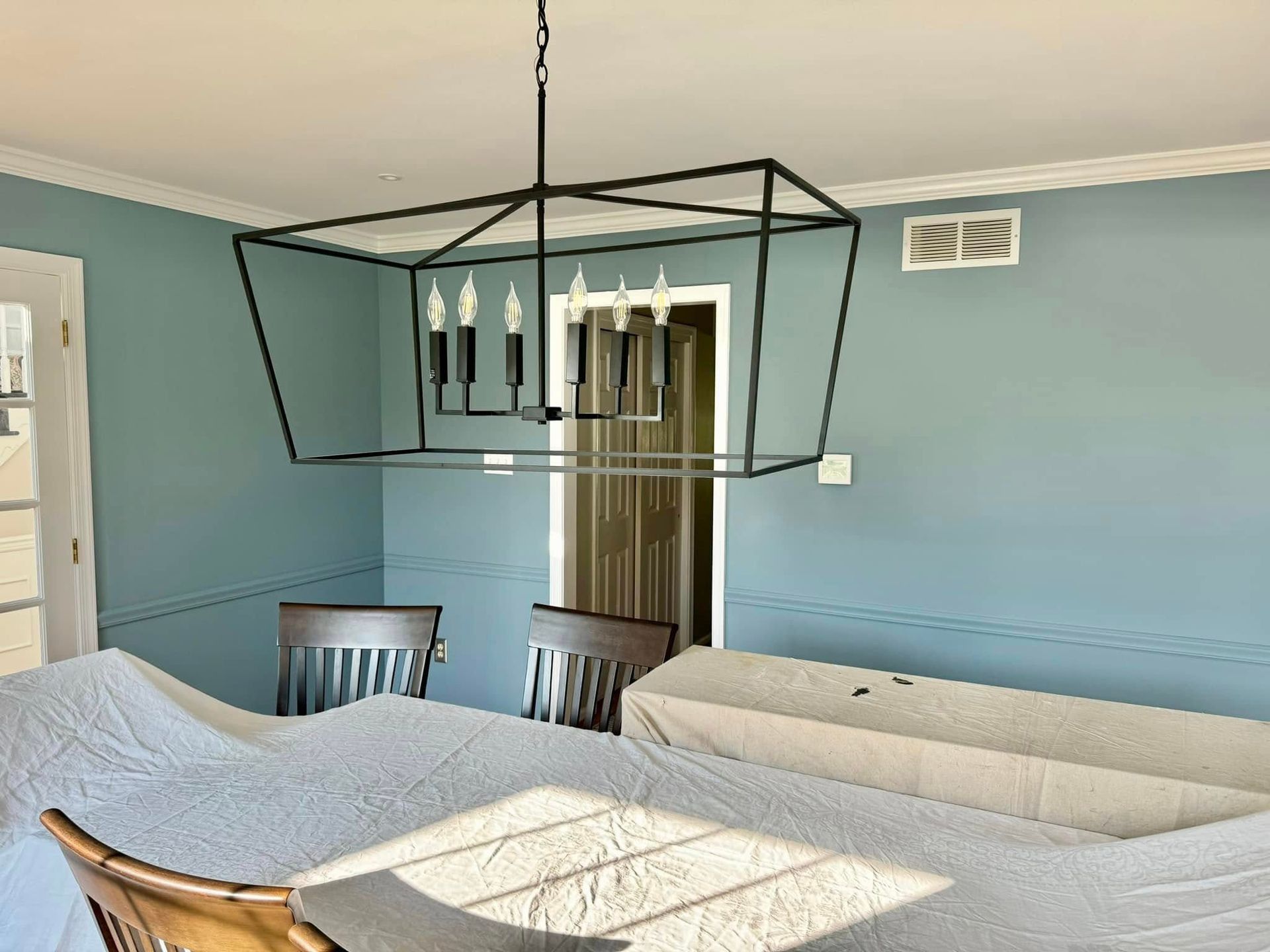 Dining room with a long table covered in white fabric, a black geometric chandelier, and teal walls.