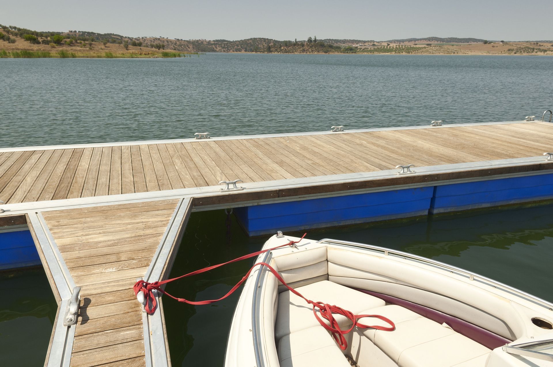 Boat tied to a wooden dock on a lake; blue water, blue dock supports, green shore in background.