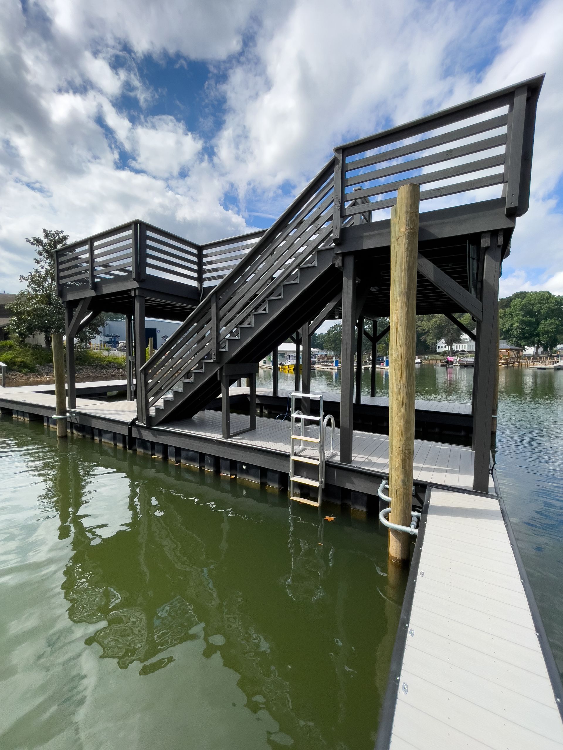 Black wooden dock structure with stairs leading to an upper platform on a body of water.