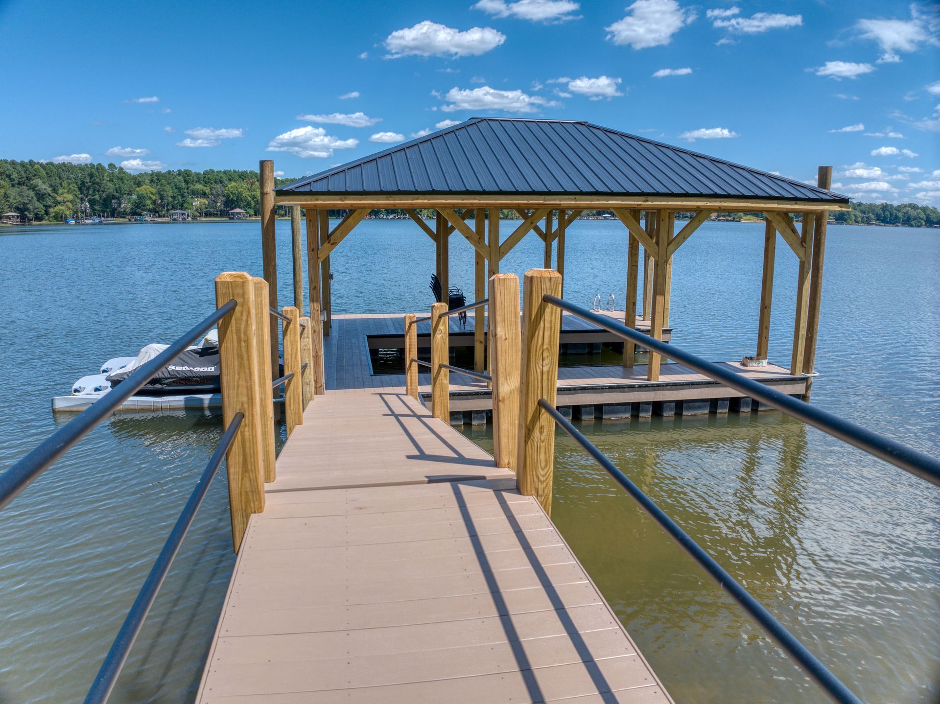 Wooden dock leads to a covered gazebo on a lake, with blue water and sky.