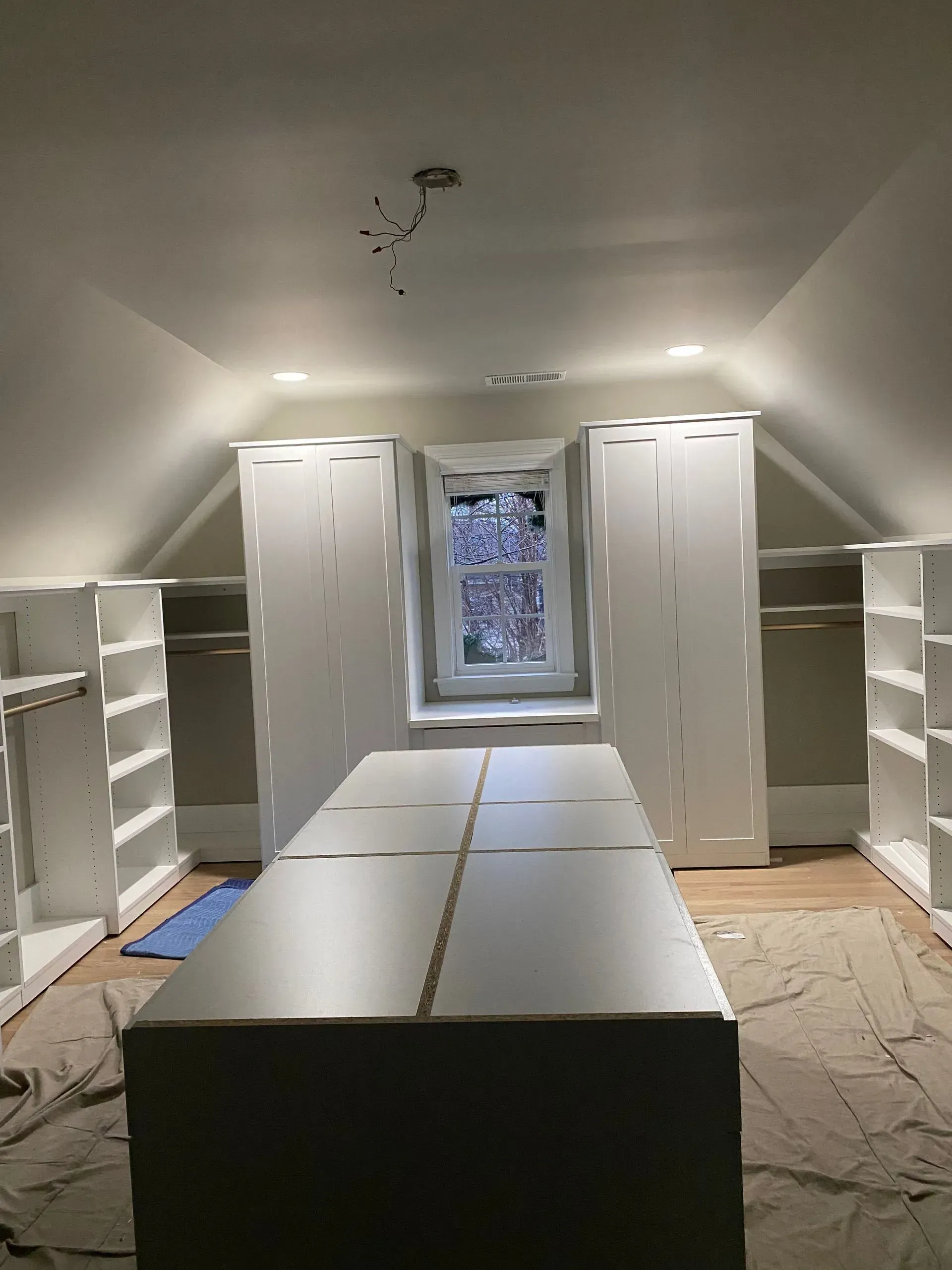 White custom closet under sloped ceiling with island and window.
