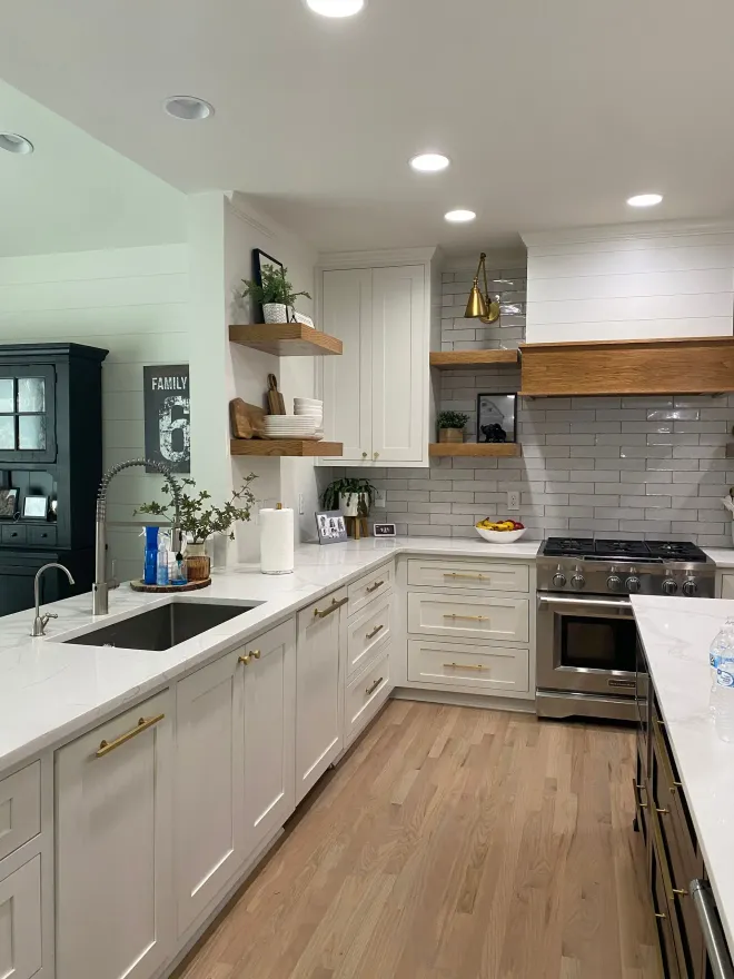 White kitchen with light wood floors, white cabinets, stainless steel appliances, and a wooden range hood.