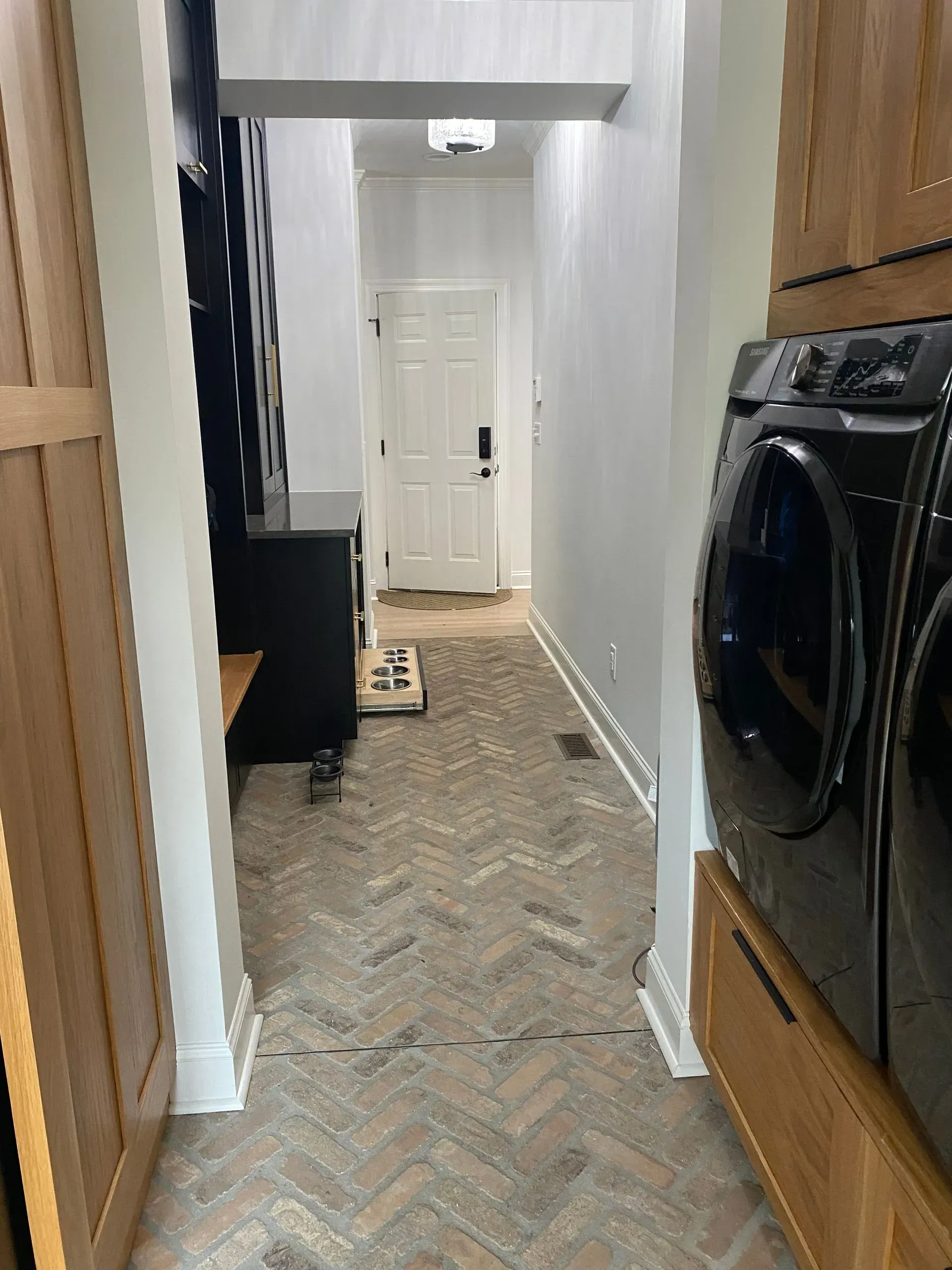 Hallway with herringbone brick floor, white walls, and black washer/dryer on the right.