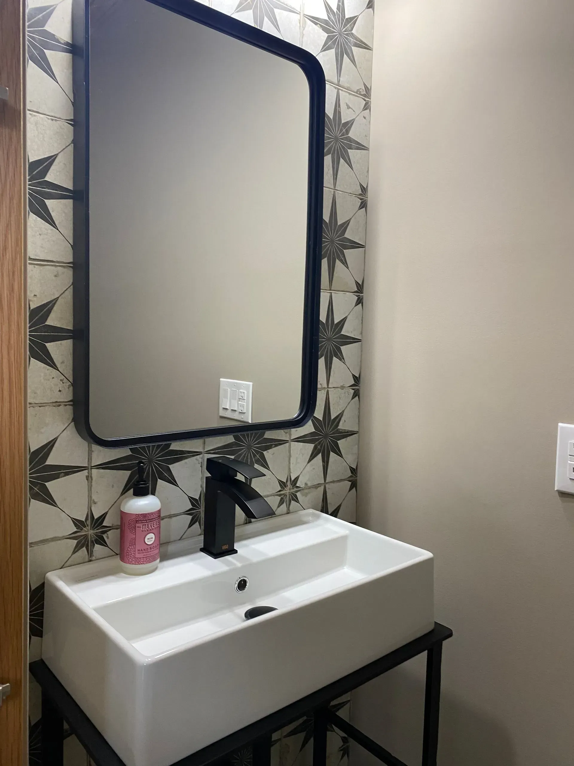 Modern bathroom with black faucet, white sink, black-framed mirror, and star tile backsplash.