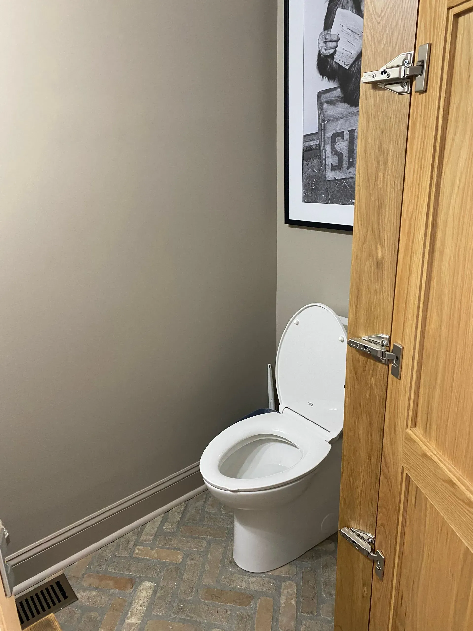 A toilet in a small room next to a wooden door with black and white art on the wall.