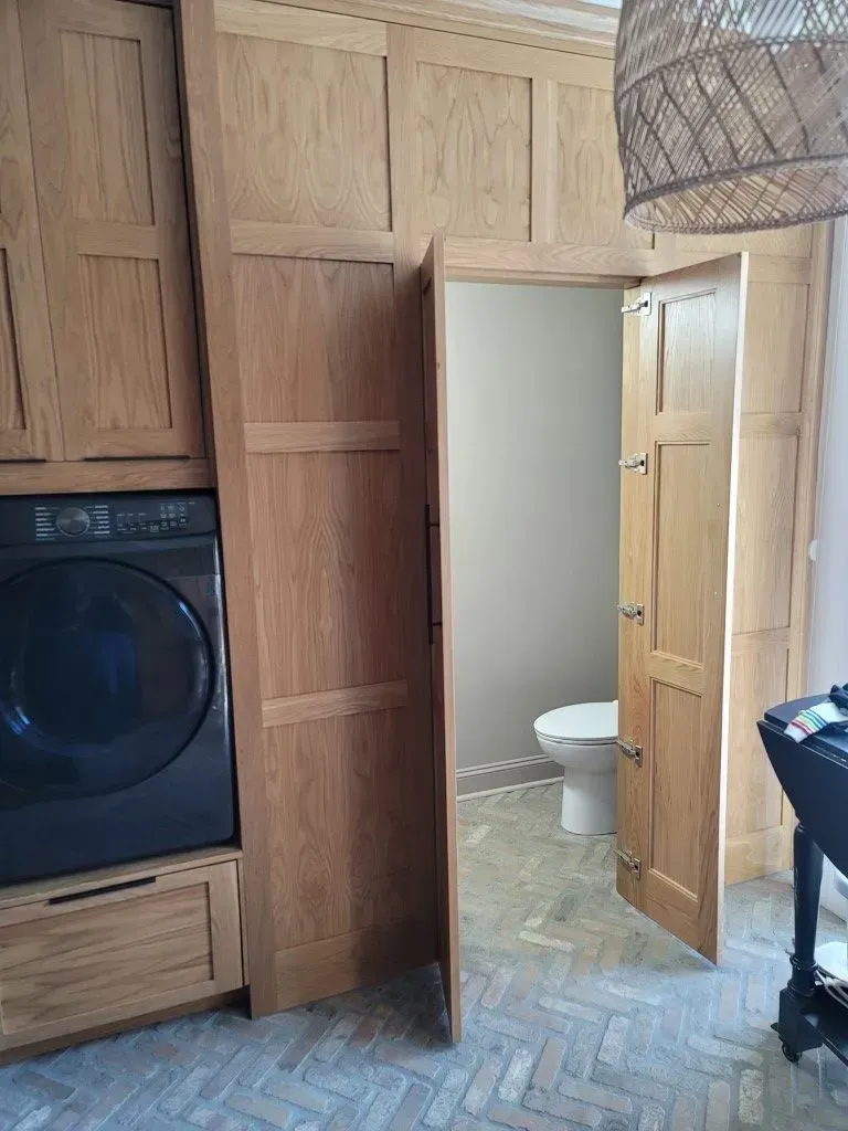 Laundry room with oak cabinetry, washer, and bathroom door open to show toilet.