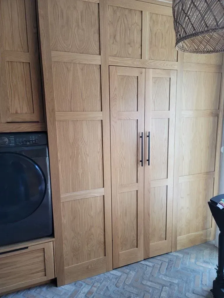 Wooden cabinet doors in a laundry room, with a dark washing machine and a woven light fixture.