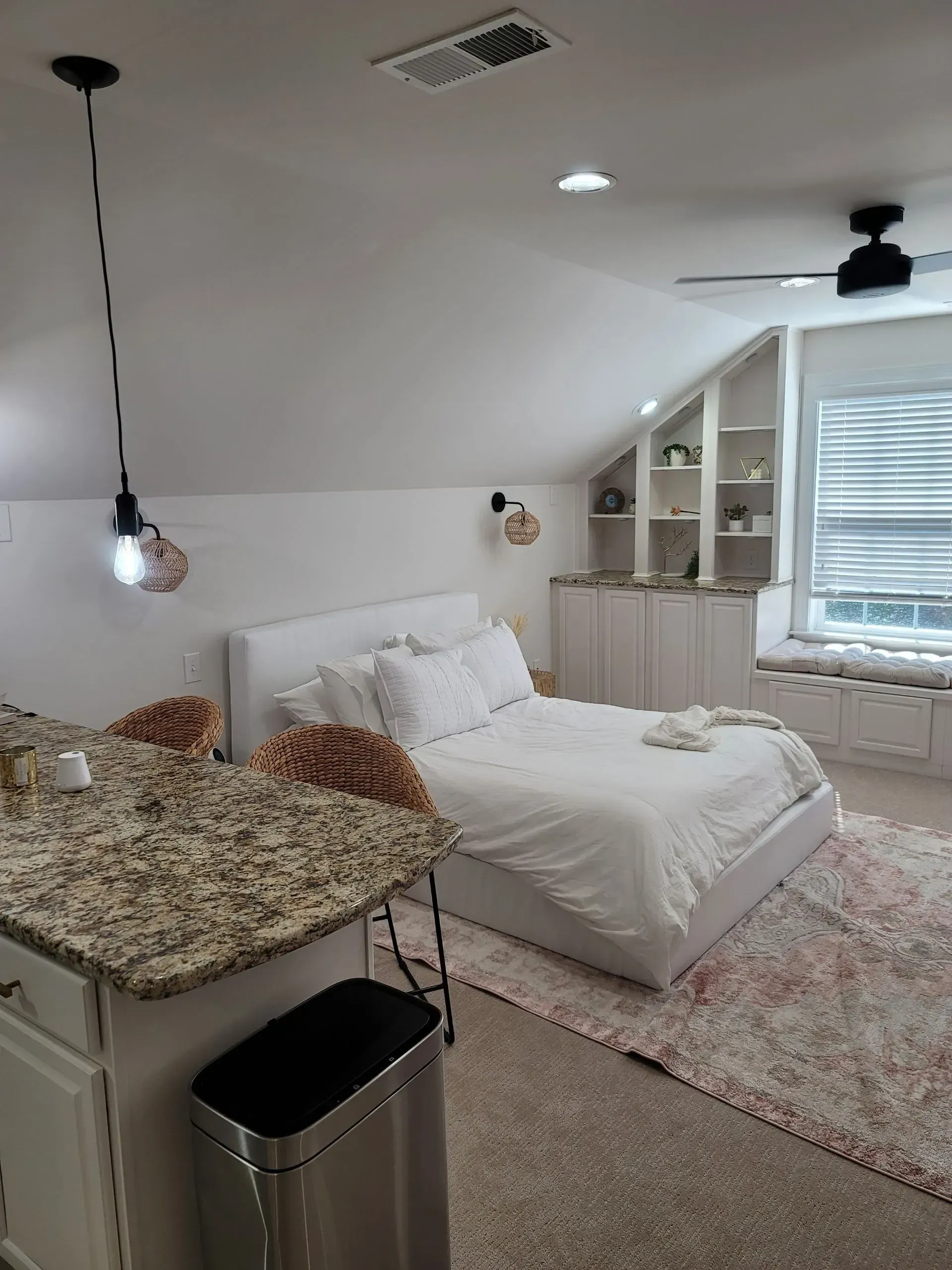 Bedroom with white bed, built-in shelves, granite countertop, and sloped ceiling.