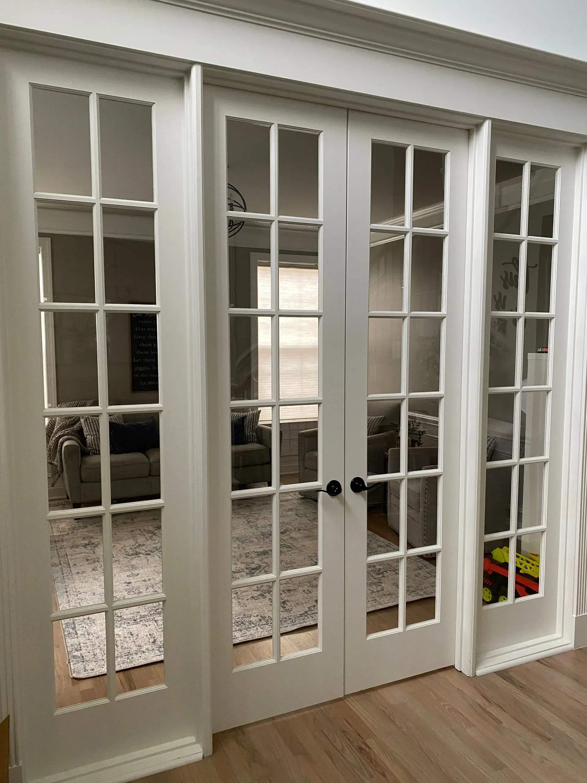 White French doors with glass panes lead to a living room with a neutral color palette.