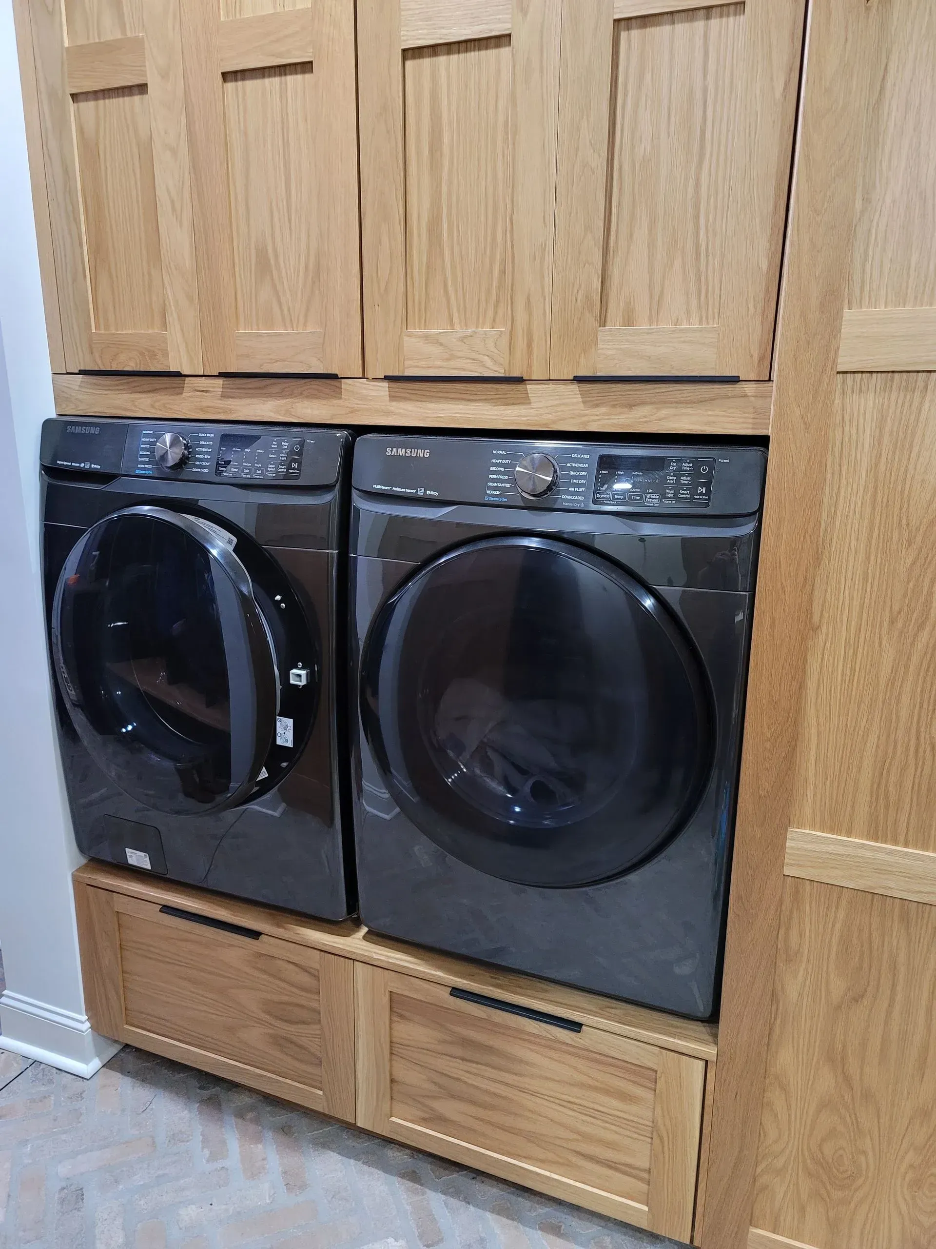 A washer and dryer set in a laundry room, enclosed in wooden cabinetry with drawers.