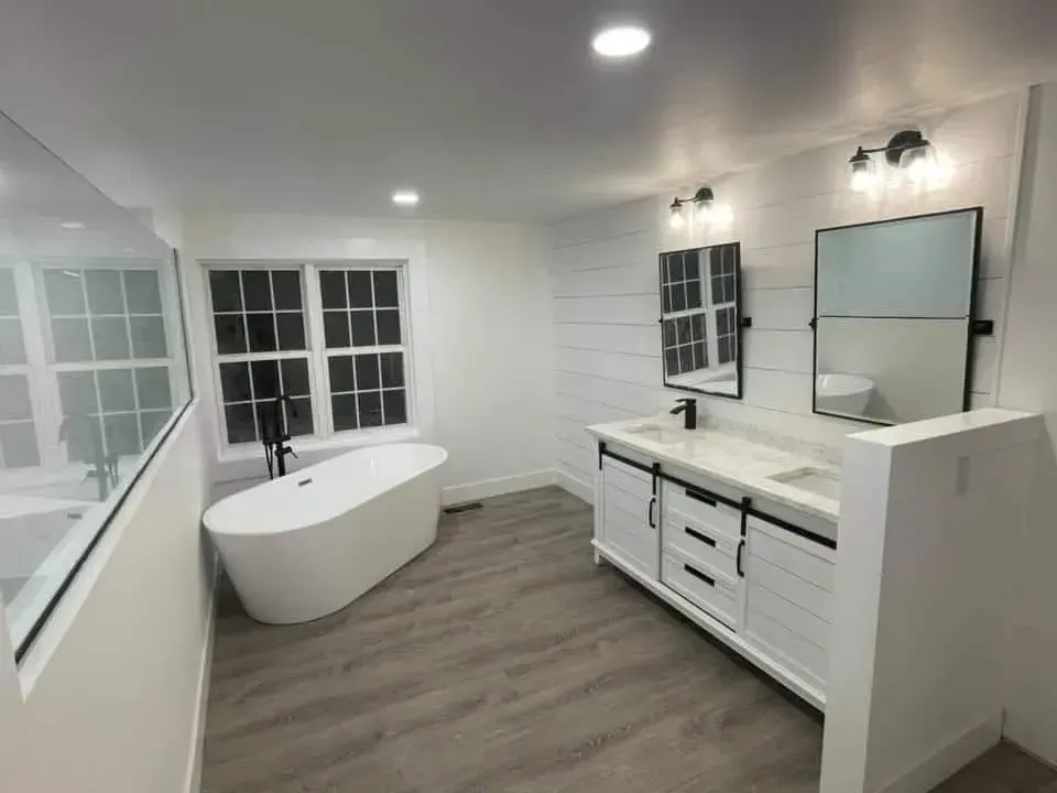 Modern white bathroom with freestanding tub, double vanity, and large window.