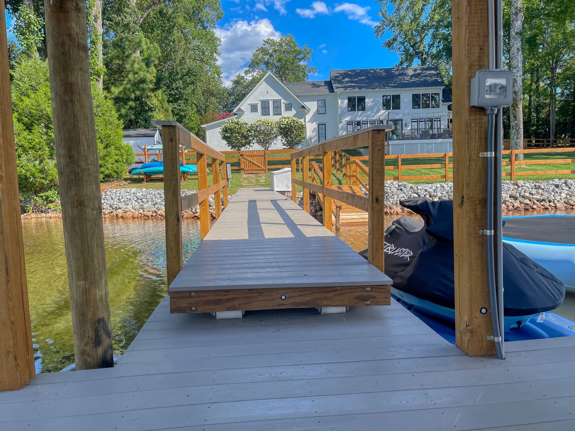 Wooden dock leading to a lake, with a house in the background and a jet ski on the right.