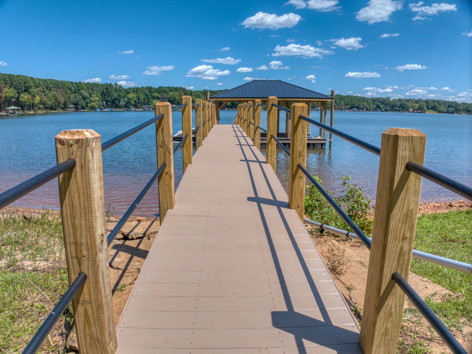 Wooden dock extending to a covered boat slip on a lake, blue sky overhead.