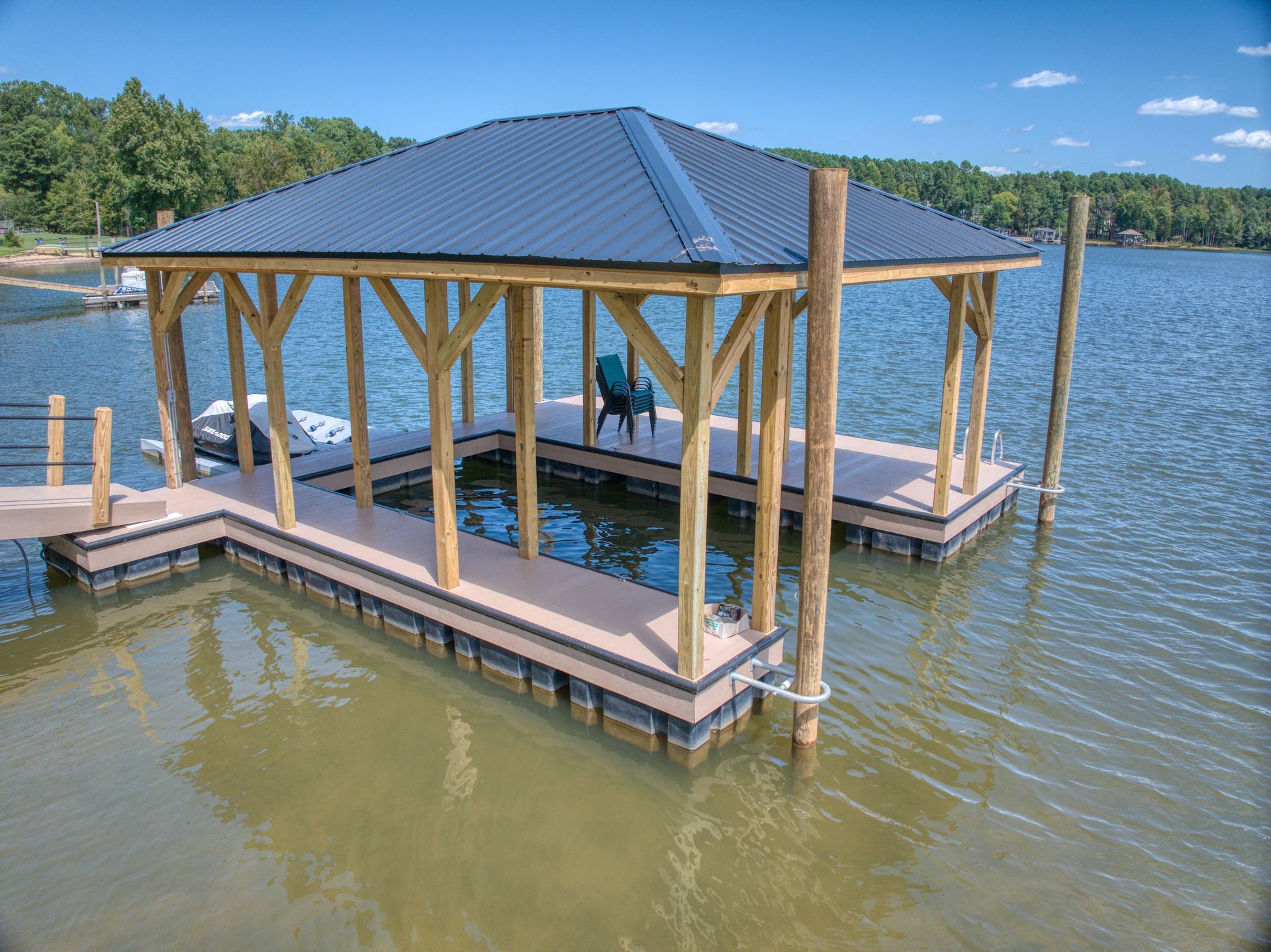 Dock with a gazebo-style roof on a lake. Brown deck and posts, blue roof, chair visible inside.