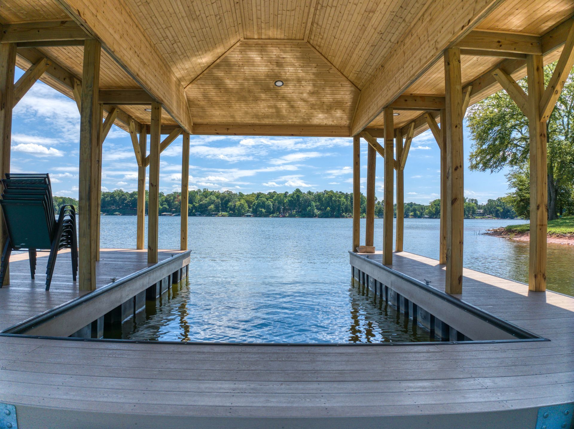 Dock with wooden supports and roof, over a lake with trees on the far shore.