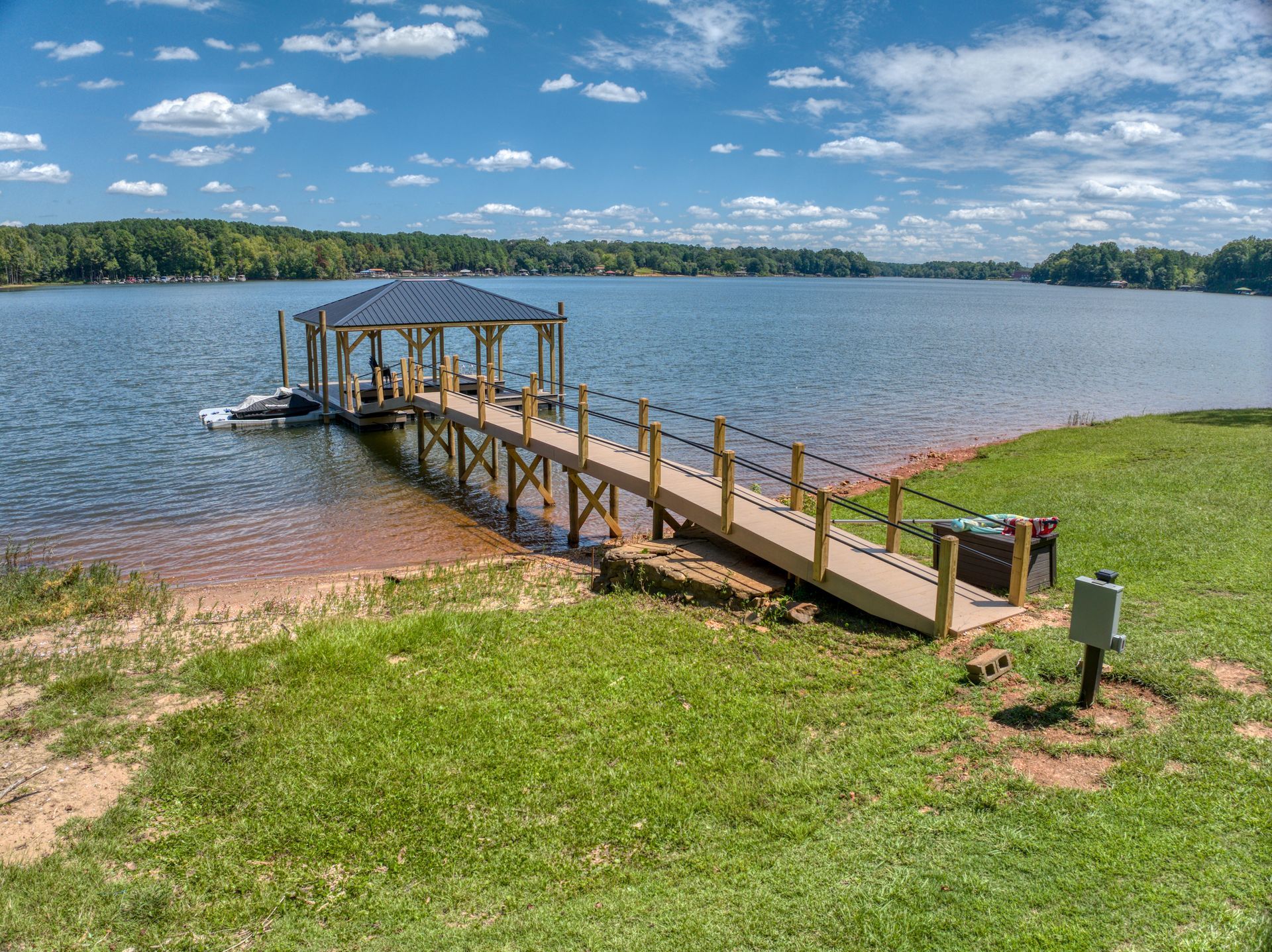 A wooden dock with gazebo extends into a lake on a sunny day with blue sky and shoreline.
