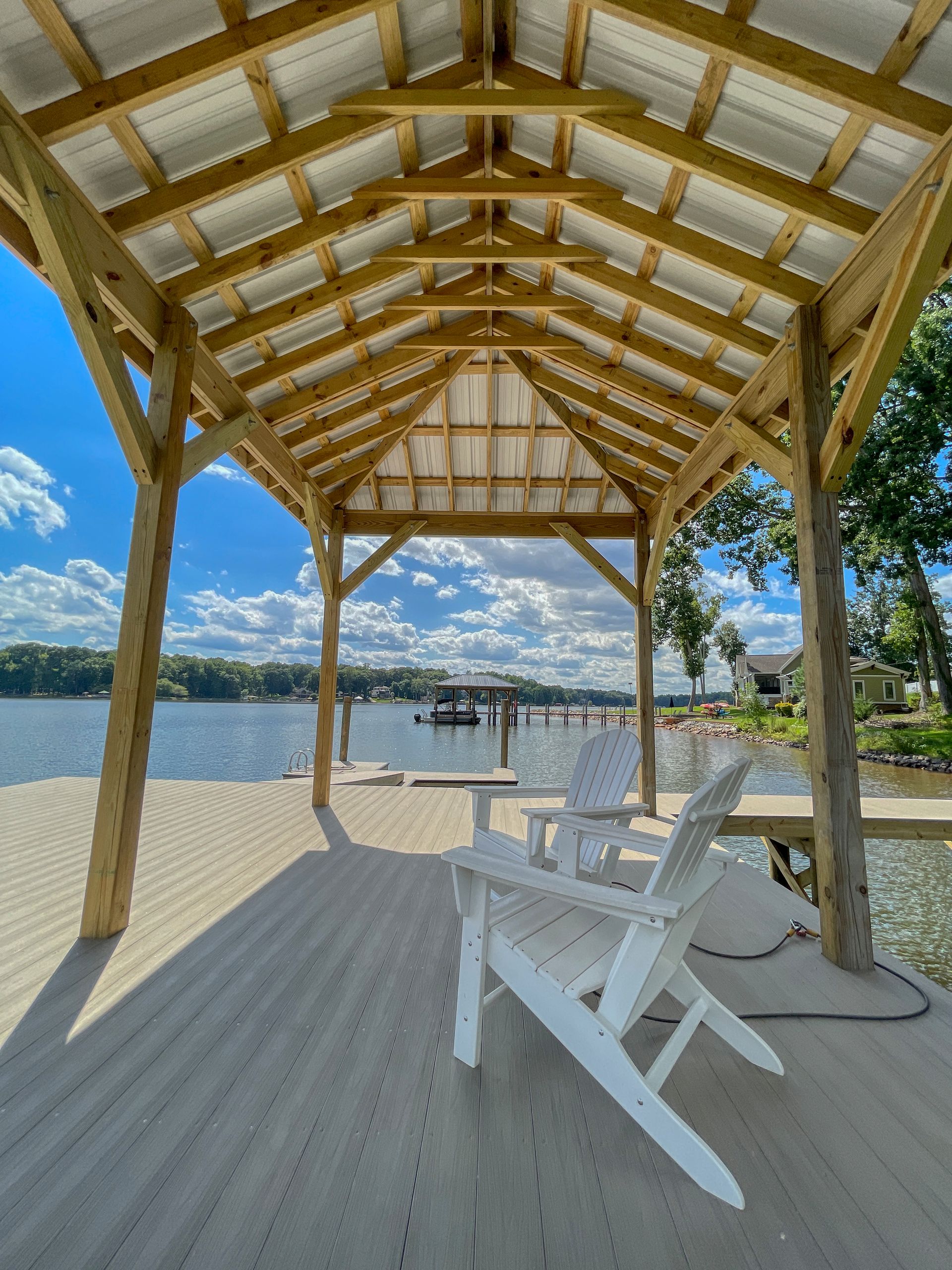 Wooden dock shelter with two white chairs overlooking a lake on a sunny day.
