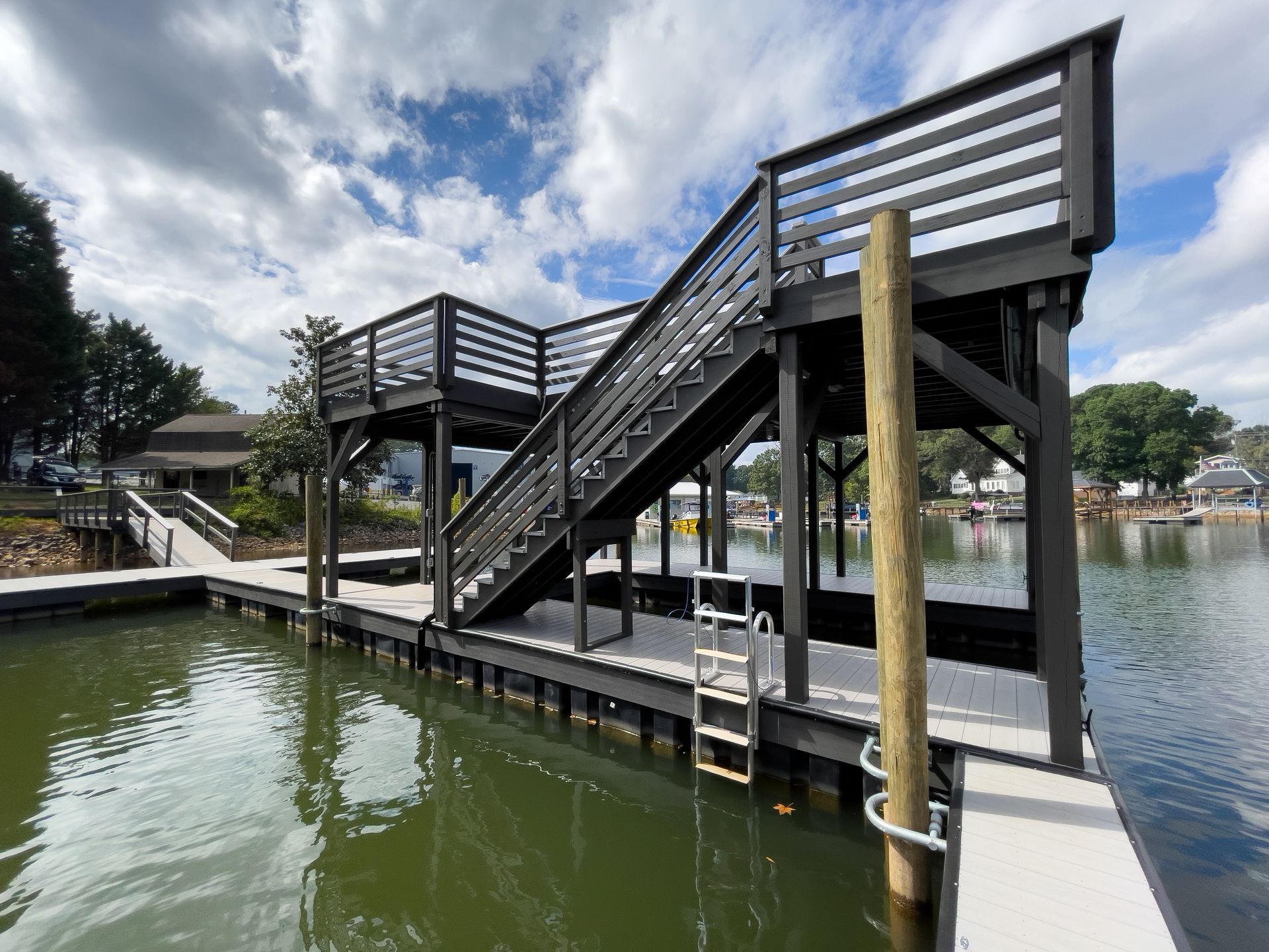 Black dock with stairs and platform over water, cloudy sky backdrop.