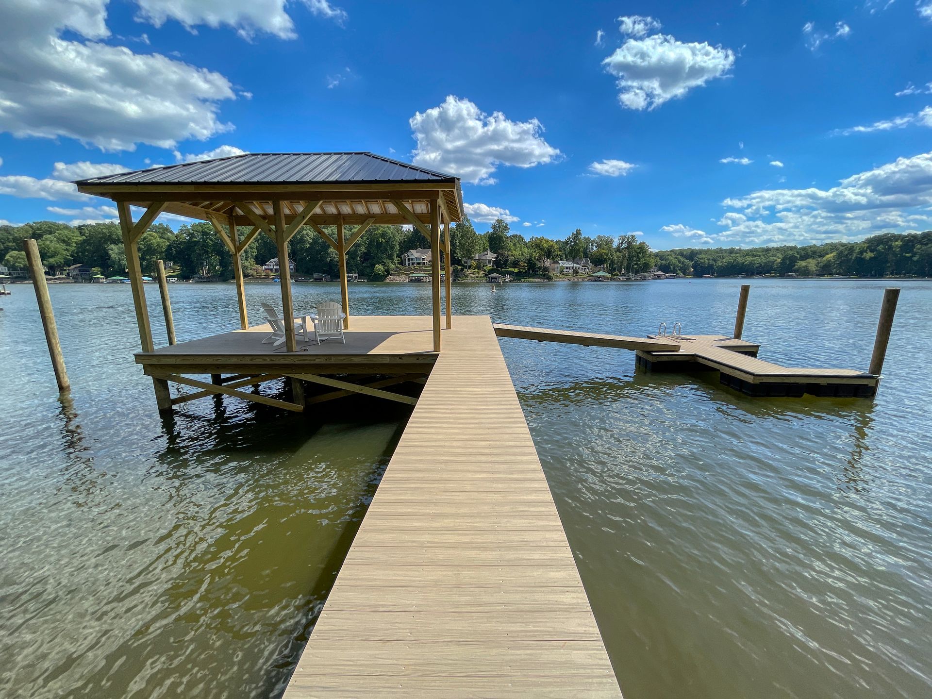 Wooden dock with gazebo on lake, sunny day, blue sky, trees in background.