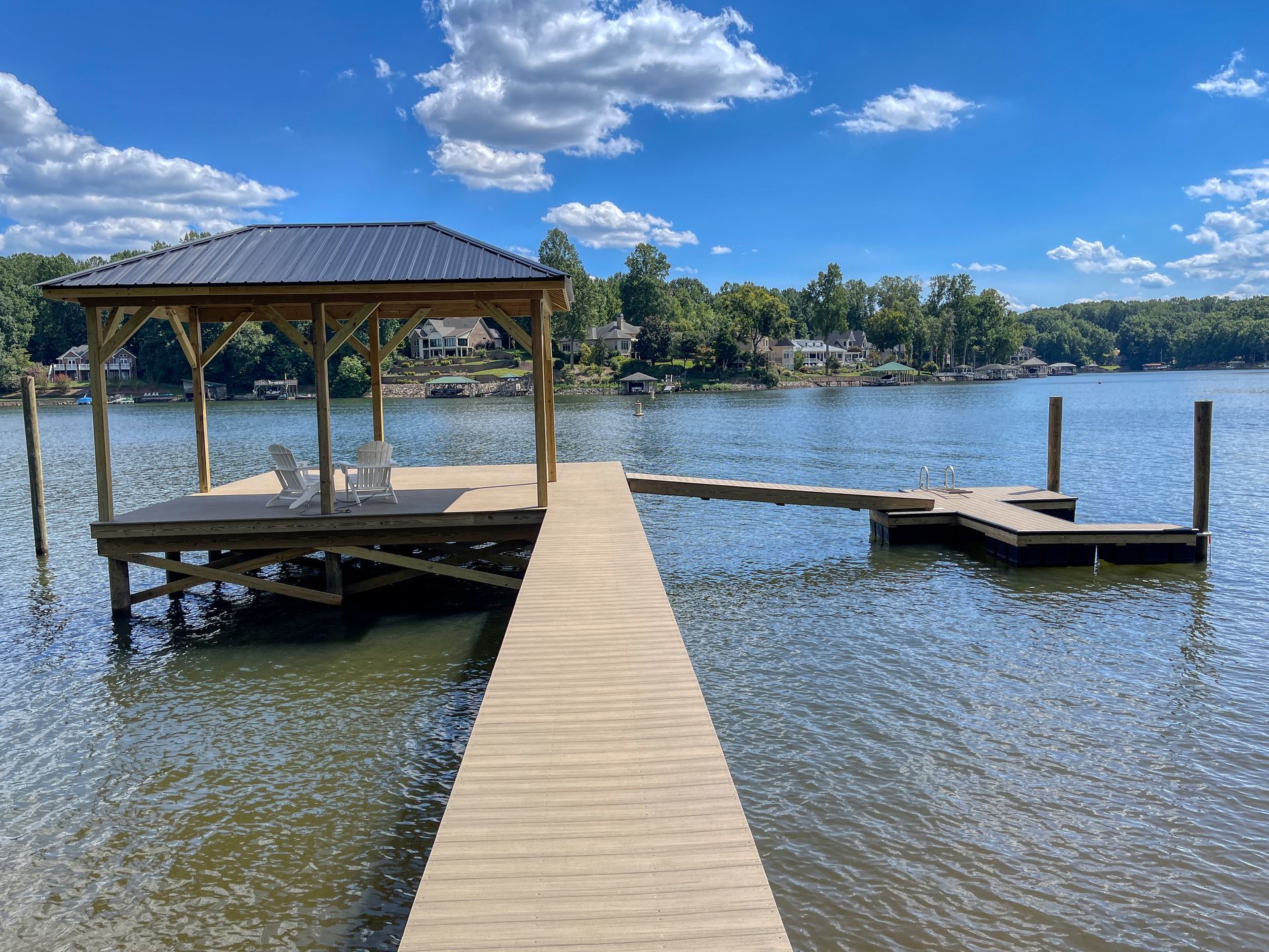 Wooden dock with gazebo on a lake, under a blue sky with clouds.