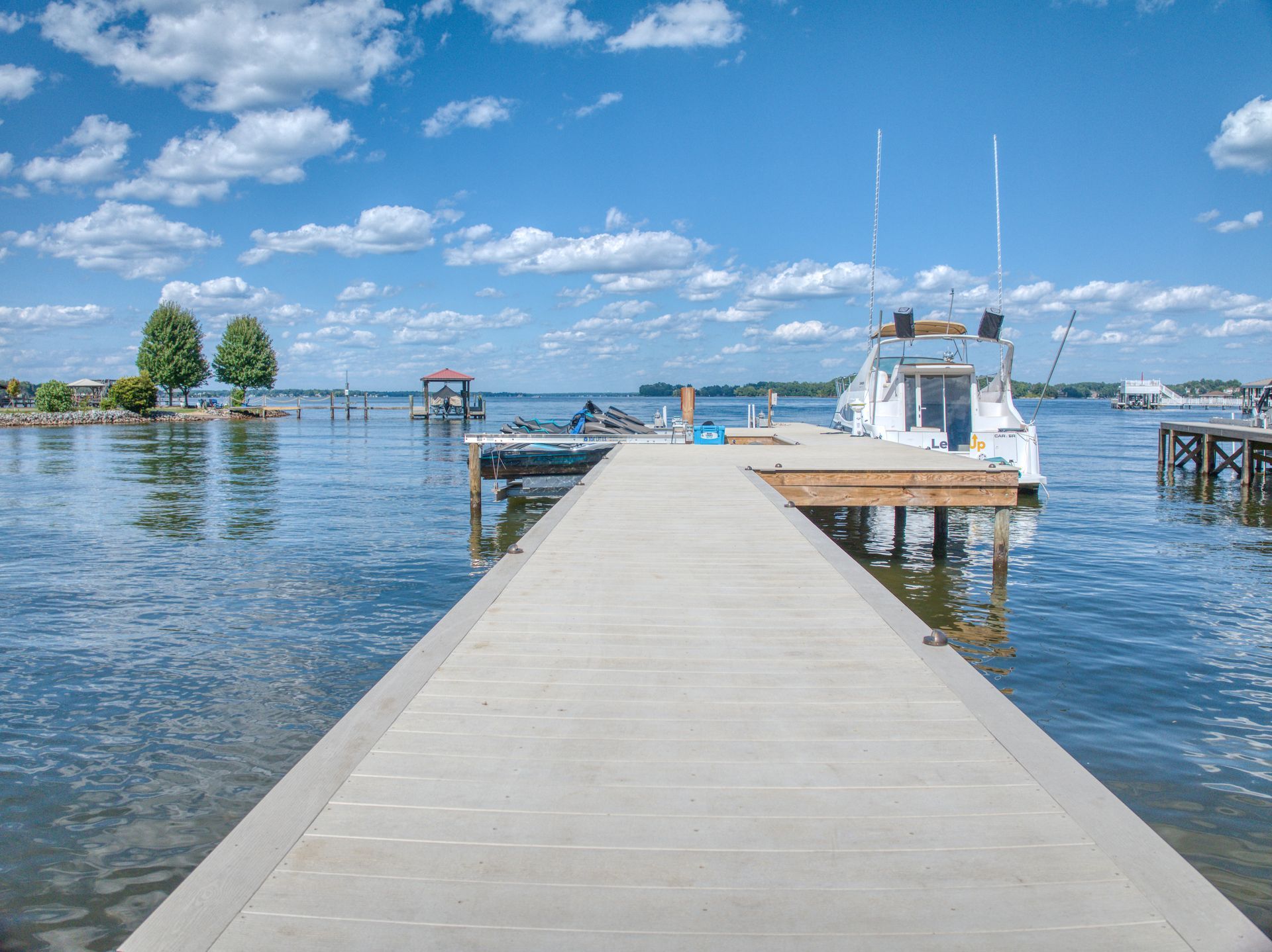 Wooden pier extends into a calm lake with a boat docked. Bright blue sky with clouds.