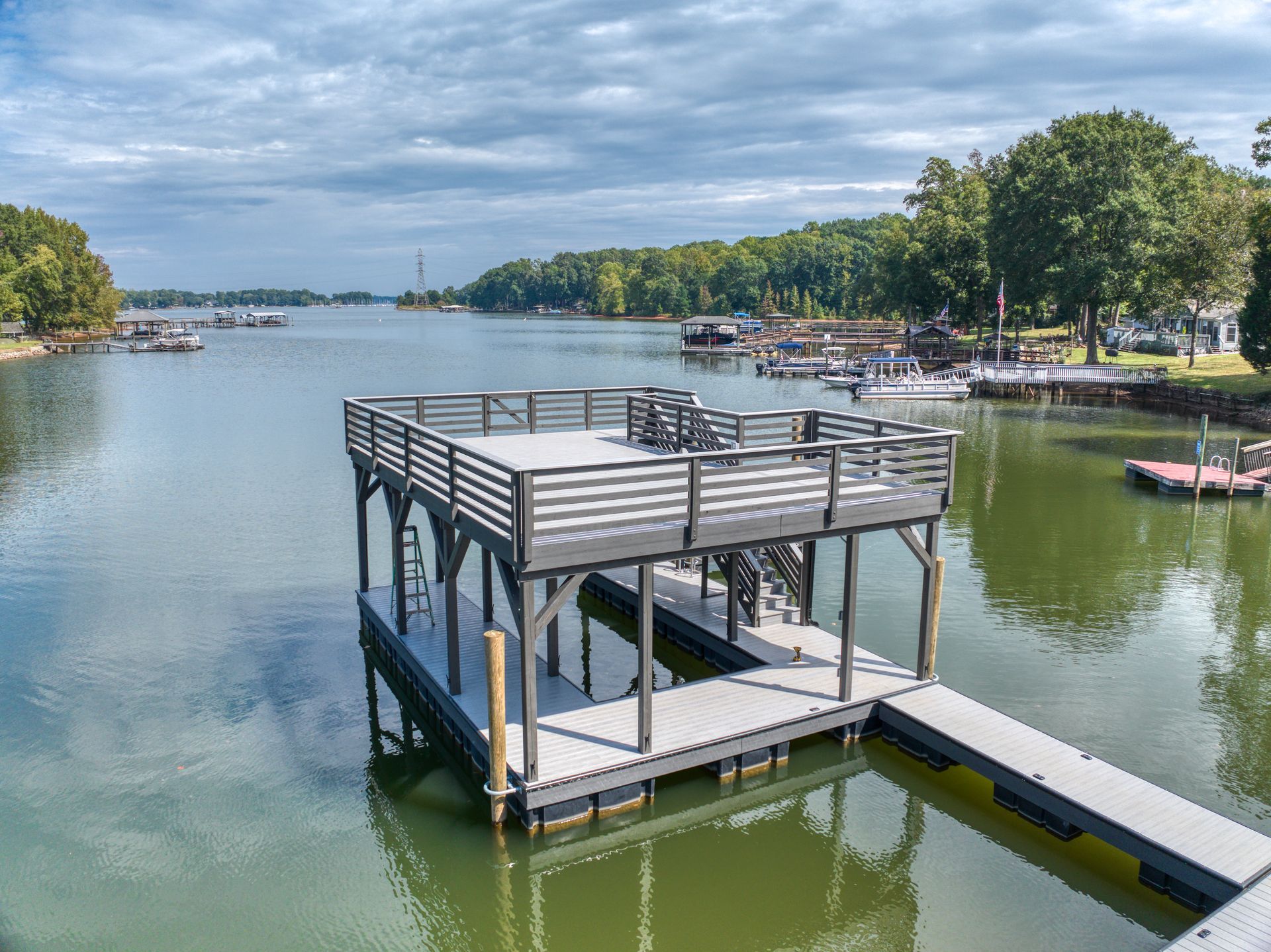 Dock over water with observation deck; boats and trees in background. Cloudy sky.